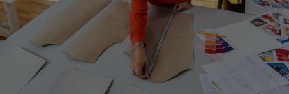 Person in an orange sweater measuring a clothing pattern panel with a tape measurer